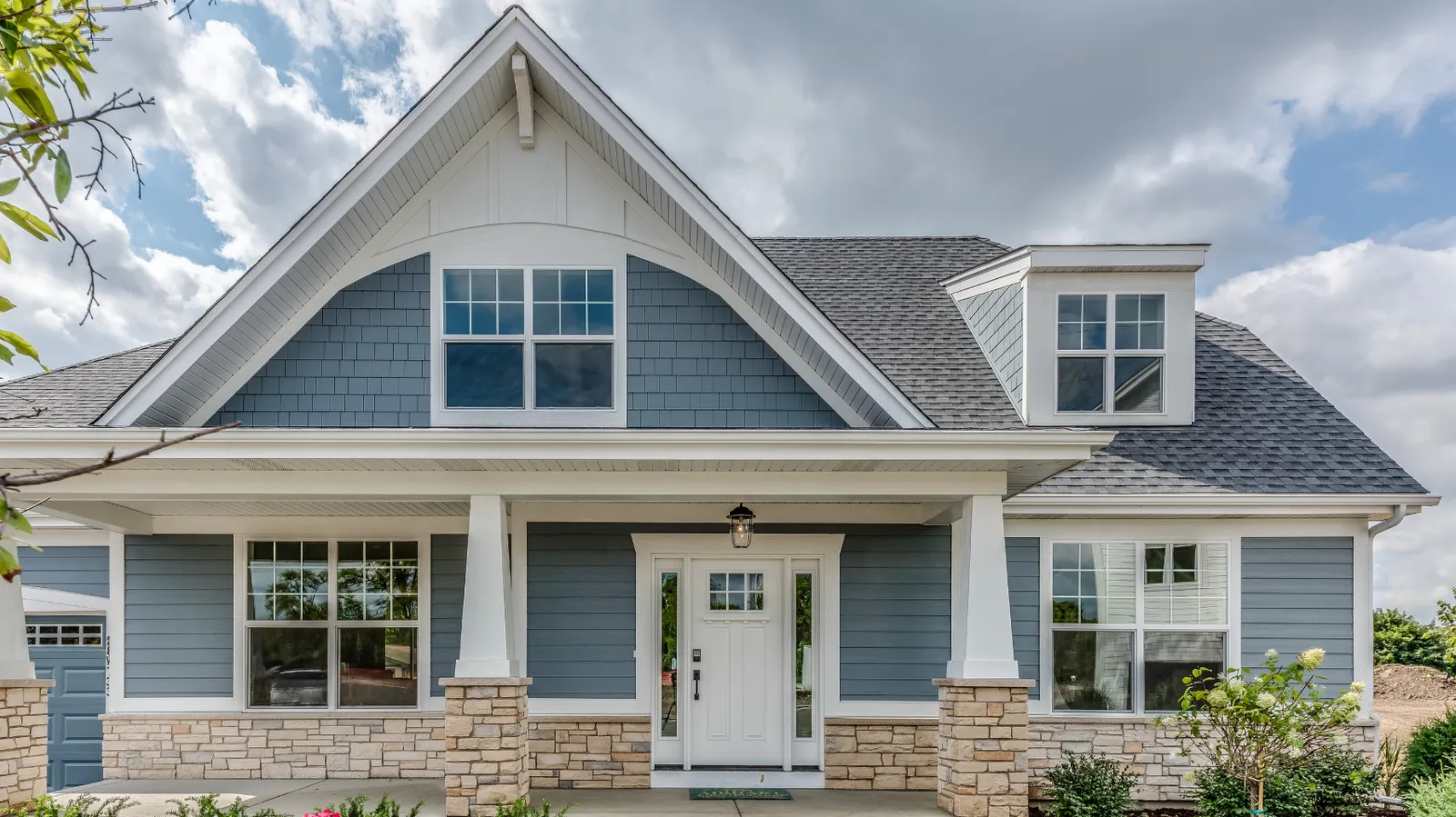 Stone porch columns on a blue craftsman home with a gray shingle roof